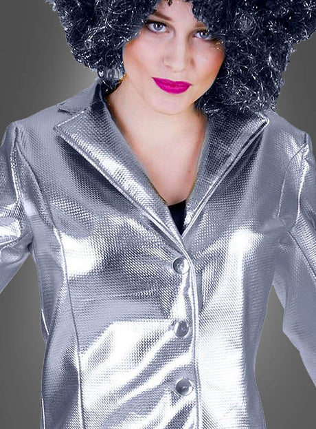 Eine Person, die eine „Glänzende Disco Jacke Damen“ in Gold oder Silber mit glänzender, silberner Struktur trägt, dazu eine schwarze Lockenperücke und knallpinken Lippenstift, vor einem grauen Hintergrund stehend.