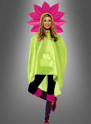 Eine Person, die ein „Pink Blume Regencape“ in Grün, schwarze Leggings, rosa Stulpen, gepunktete Stiefel und einen rosa Blumenkopfschmuck – gestaltet als verspieltes „Flower Power“-Accessoire – trägt, steht vor einem grauen Hintergrund mit Farbverlauf.