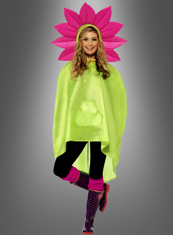 Eine Person, die ein „Pink Blume Regencape“ in Grün, schwarze Leggings, rosa Stulpen, gepunktete Stiefel und einen rosa Blumenkopfschmuck – gestaltet als verspieltes „Flower Power“-Accessoire – trägt, steht vor einem grauen Hintergrund mit Farbverlauf.