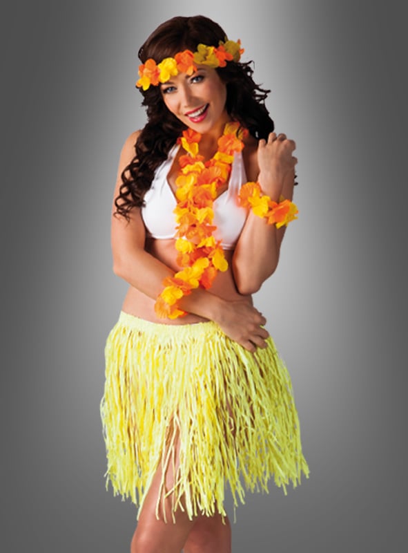 Eine Frau, die ein weißes Bikini-Oberteil und das „Hula Hawaii“-Set mit Bastrock trägt – bestehend aus einem gelben Grasrock sowie einem dazu passenden gelb-orangefarbenen Blumen-Lei, einem Armband und einem Stirnband –, steht vor einem grauen Hintergrund mit Farbverlauf.