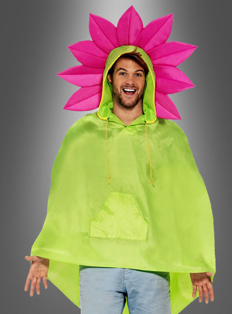 Eine Person, die das „Pink Blume Regencape“ in Grün trägt – mit einer großen, blumenförmigen Kapuze in Rosa –, lächelt vor einem grauen Hintergrund.
