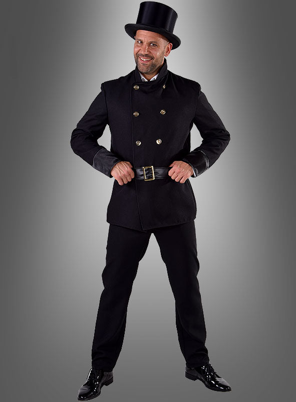 Ein Mann im Schornsteinfeger-Herrenkostüm – bestehend aus einem schwarzen Zweireiher, einer passenden Hose, einem Zylinder und schwarzen Schuhen – steht vor einem grauen Hintergrund mit Farbverlauf und lächelt.