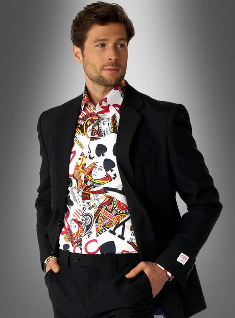 Ein Mann in einem schwarzen Anzug trägt ein auffälliges Spielkarten-Hemd von OppoSuits, dessen Muster aus Spielkarten besteht, und steht vor einem grauen Hintergrund mit Farbverlauf.