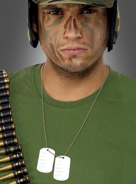 Eine Person mit Tarnbemalung im Gesicht und in Uniform trägt Erkennungsmarken und einen Patronengurt über einem grünen Hemd und blickt geradeaus.