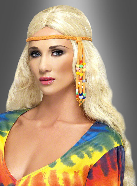 Eine Frau mit langen blonden Haaren, die ein buntes Tie-Dye-Oberteil und ein geflochtenes orangefarbenes Hippie-Stirnband mit Perlen trägt, posiert vor einem grauen Hintergrund mit Farbverlauf.