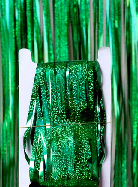 Vor dem „Lametta Vorhang 200–250 cm Party Deko“ in passendem Grün liegt eine Rolle glänzendes grünes Lametta-Band, das mit seinem schillernden Glanz die perfekte Partydekoration bildet.