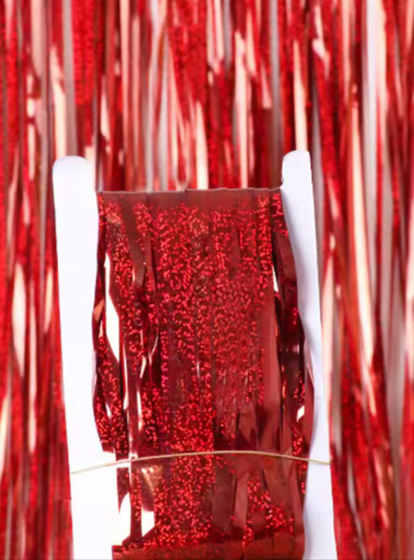 Eine Rolle rote Metallic-Lametta-Fransen wird mit einem Gummiband aufrecht gehalten, während im Hintergrund passende „Lametta Vorhang 200–250 cm Party Deko“-Lametta hängt und für eine festliche Note sorgt.