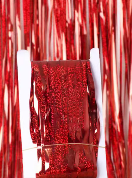 Eine Rolle rote Metallic-Lametta-Fransen wird mit einem Gummiband aufrecht gehalten, während im Hintergrund passende „Lametta Vorhang 200–250 cm Party Deko“-Lametta hängt und für eine festliche Note sorgt.