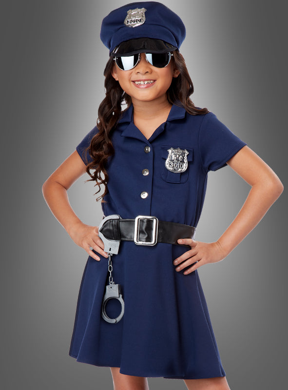 Ein Kind trägt das „Polizistin“-Mädchenkostüm „US Cop“ in Marineblau, komplett mit Mütze, Sonnenbrille, Dienstmarke, schwarzem Gürtel und Handschellen, und steht selbstbewusst vor einem grauen Hintergrund.