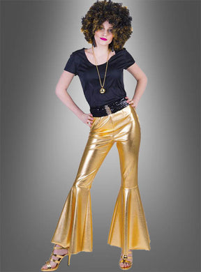 Eine Person steht mit den Händen in den Hüften vor einem grauen Hintergrund und trägt ein schwarzes Oberteil, die „Deluxe Damen Schlaghose“ – eine goldene Disco-Schlaghose –, goldene High Heels und eine lockige Perücke – ein kultiges Disco-Outfit aus den 70er Jahren.