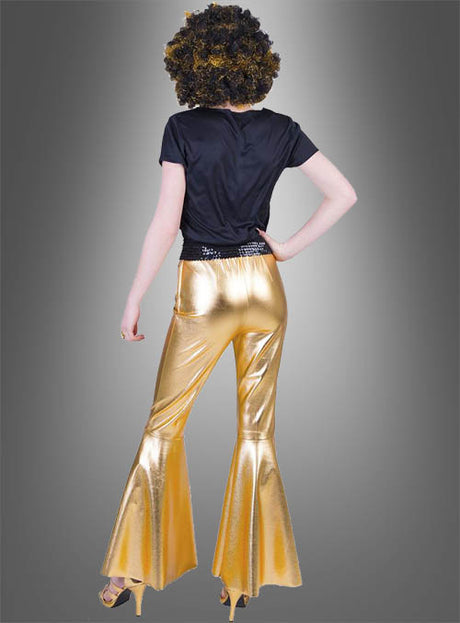 Eine Person steht mit dem Rücken zur Kamera und trägt ein schwarzes Shirt, goldene High Heels, eine lockige Perücke und die „Deluxe Damen Schlaghose Gold Disco“ – vor einem grau verlaufenden Hintergrund wird so ein klassisches Disco-Outfit der 70er Jahre perfekt in Szene gesetzt.