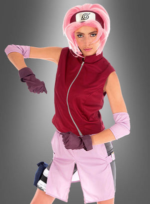 Eine Person mit einer rosa Perücke und einer roten Weste posiert im Sakura-Kostüm aus „Naruto Shippuden“, komplett mit Handschuhen, einem Stirnband mit dem Blatt-Symbol und hellrosa Shorts, die an den ikonischen Look von Sakura Haruno erinnern.