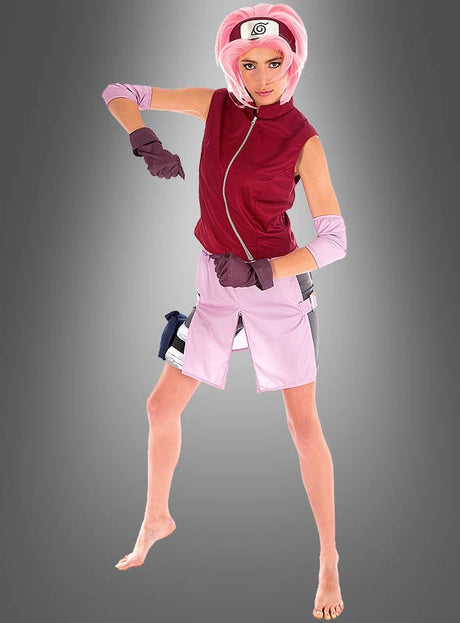 Eine Person, die das Sakura-Kostüm aus „Naruto Shippuden“ trägt – komplett mit Stirnband, Handschuhen und Armstulpen –, posiert barfuß vor einem grauen Hintergrund mit Farbverlauf und verkörpert damit perfekt Sakura Haruno.