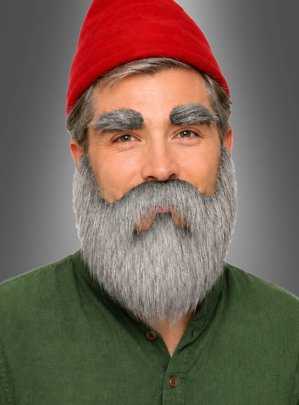 Ein Mann mit grauem Bart und dichten grauen Augenbrauen aus dem „Vollbart-Set mit Augenbrauen“, der einen roten Hut und ein grünes Hemd trägt, posiert vor einem neutralen grauen Hintergrund und verkörpert perfekt den Look eines Zwerg-Kostüms.