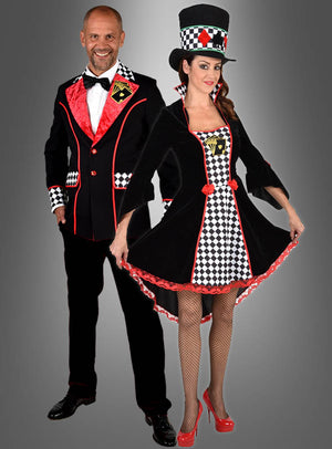 Eine Frau trägt das „Deluxe Poker Face“-Samtkleid, ein Damen-Karnevalskostüm im Kleidstil mit passendem Zylinder, während der Mann neben ihr in Anzug und Fliege posiert; beide sind in aufeinander abgestimmten Kostümen mit schwarz-rot-weißem Schachbrettmuster vor einem grauen Hintergrund gekleidet.