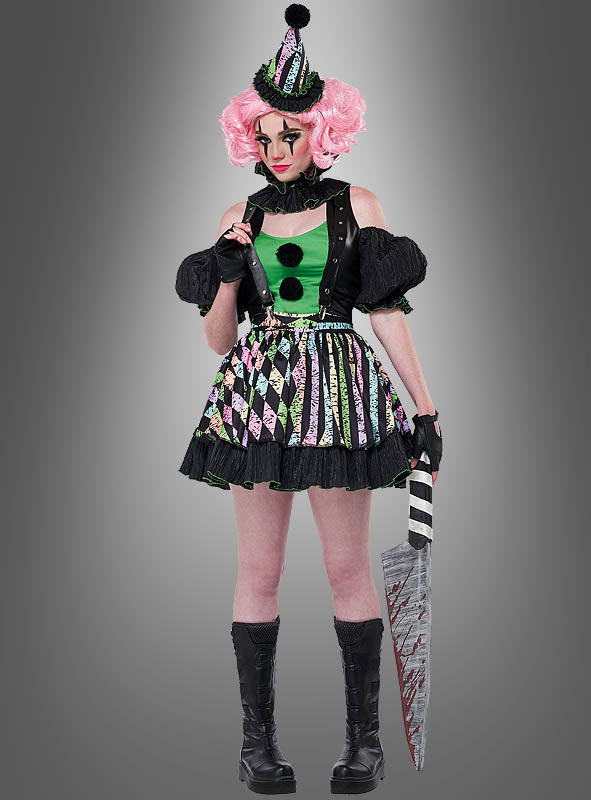 Eine Person, die das Damenkostüm „Verrückte Clownfrau Nicky“ trägt – bestehend aus einem bunten Clown-Outfit und einer rosa Perücke –, hält ein großes, blutiges Requisitenmesser in der Hand, während sie vor einem grauen Hintergrund steht.