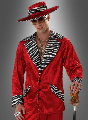 Ein Mann im „Zuhälter-Outfit in Rot mit Zebramuster“: ein leuchtend roter Anzug mit Details im Zebramuster, ein breitkrempiger Hut, überdimensionaler Goldschmuck, eine Sonnenbrille und ein Spazierstock mit der Aufschrift „PIMP“ vor grauem Hintergrund – ein kultiger Retro-Look, perfekt für jede 70er-Jahre-Party oder jede Themenveranstaltung.