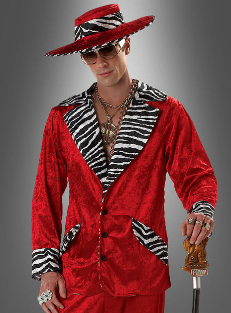 Ein Mann im „Zuhälter-Outfit in Rot mit Zebramuster“: ein leuchtend roter Anzug mit Details im Zebramuster, ein breitkrempiger Hut, überdimensionaler Goldschmuck, eine Sonnenbrille und ein Spazierstock mit der Aufschrift „PIMP“ vor grauem Hintergrund – ein kultiger Retro-Look, perfekt für jede 70er-Jahre-Party oder jede Themenveranstaltung.