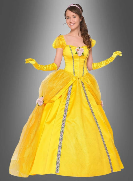 Eine Frau, die das „Die Schöne Belle“-Ballkostüm für Damen trägt – ein gelbes Ballkleid mit Blumenverzierungen und langen gelben Handschuhen –, steht lächelnd vor einem grauen Hintergrund.