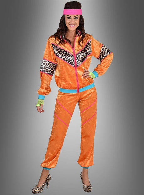 Eine Frau in einem XXL-Trainingsanzug im 80er-Jahre-Look in leuchtendem Orange mit Leopardenmuster-Details, kombiniert mit einem rosa Stirnband und passenden High Heels mit Leopardenmuster, steht lächelnd vor einem grauen Hintergrund – eine ideale Wahl für eine authentische 80er-Jahre-Party oder als auffälliges 80er-Jahre-Outfit.