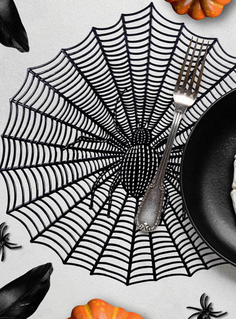 Eine Halloween-Tischunterlage in verschiedenen Designs im dekorativen schwarzen Spinnennetz-Stil dient als Platzset und eignet sich perfekt für Halloween. Sie wird mit einer Gabel und einem schwarzen Teller darauf abgebildet, umgeben von kleinen Kürbissen, schwarzen Federn und Plastikspinnen als gruselige Motive – damit ist sie ein ideales Platzset für Halloween.