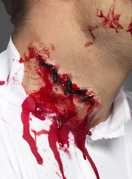 Eine Nahaufnahme des Halses einer Person zeigt künstliche blutige Wunden mit schwarzen Nähten, die mit der „Realistische genähte Latex-Wunde“ gestaltet wurden; rote Flüssigkeit tropft auf ein weißes Hemd und sorgt für ein dramatisches Special-Effects-Make-up – ideal, um jedes Zombie-Outfit abzurunden.