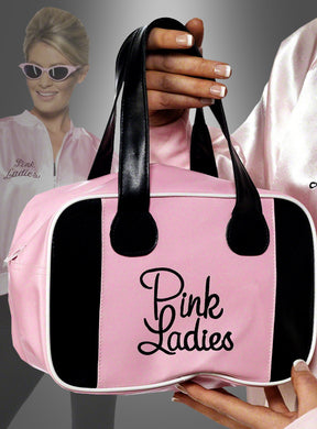 Eine Hand hält die Handtasche „Pink Ladies Grease“ – eine rosa-schwarze Tasche mit der Aufschrift „Pink Ladies“ –, die perfekt für „Grease“-Fans ist, während im Hintergrund jemand in einer passenden Jacke und mit einer rosa Sonnenbrille steht.