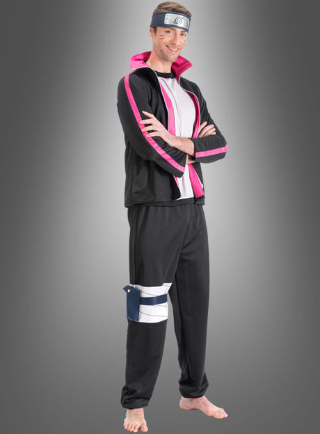 Ein Mann trägt das „Boruto“-Kostüm für Erwachsene aus „Naruto“ im Anime-Stil in Schwarz und Rosa, komplett mit Stirnband und Beutel, und steht barfuß mit verschränkten Armen vor einem grauen Hintergrund mit Farbverlauf.