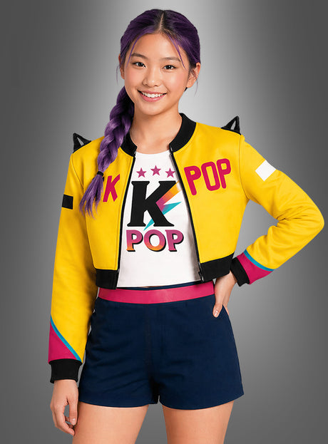 Eine lächelnde Person mit violetten Zöpfen trägt die gelbe Jacke „Sängerin Romy Kinder K-Pop Star“ und das dazu passende Shirt, dazu marineblaue Shorts, und steht vor einem grauen Hintergrund mit Farbverlauf.