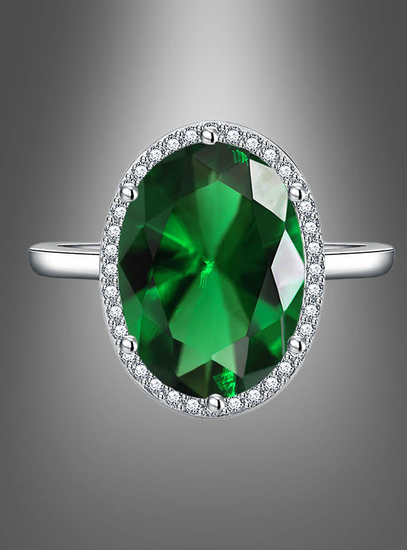 Ring mit großem Edelstein: Ein silberner Ring mit einem großen, ovalen grünen Edelstein, umgeben von kleinen klaren Steinen, präsentiert vor einem grauen Hintergrund mit Farbverlauf.