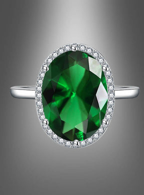 Ring mit großem Edelstein: Ein silberner Ring mit einem großen, ovalen grünen Edelstein, umgeben von kleinen klaren Steinen, präsentiert vor einem grauen Hintergrund mit Farbverlauf.