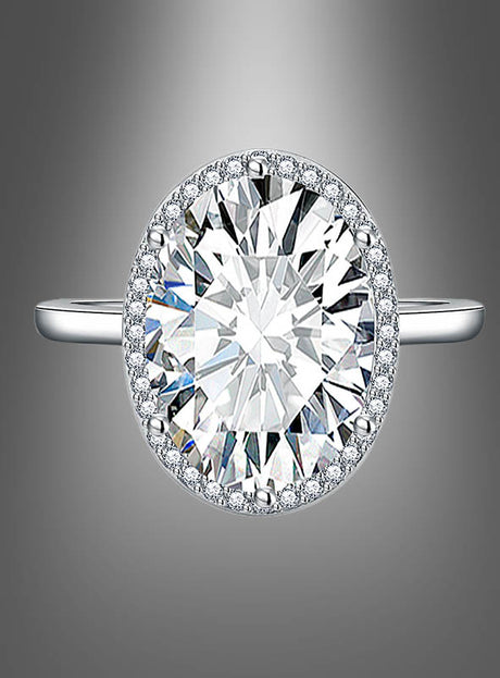 Ring mit großem Edelstein: ein silberner Ring mit einem großen ovalen Mittelstein im Diamant-Look, umgeben von einem funkelnden Halo aus kleineren Steinen, präsentiert vor einem sanft verlaufenden grauen Hintergrund.