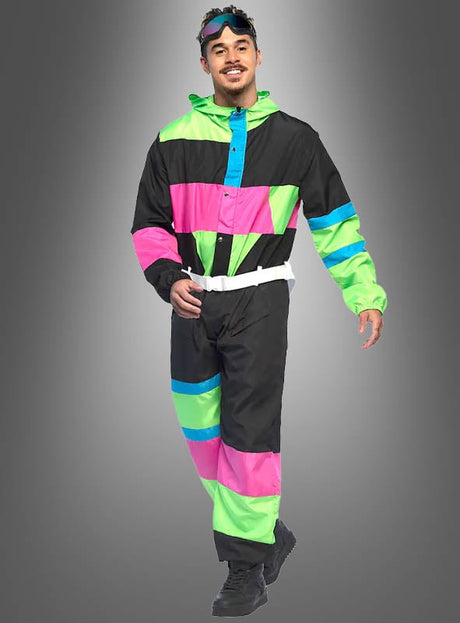 Ein Mann präsentiert den „Retro-Skianzug mit Brille“ – einen farbenfrohen Skianzug im Retro-Stil mit auffälligen grünen, blauen und pinkfarbenen Farbblöcken, einem weißen Gürtel, schwarzen Stiefeln und einer Skibrille auf dem Kopf –, während er vor einem grauen Hintergrund mit Farbverlauf entlangläuft – ideal als Après-Ski-Outfit.