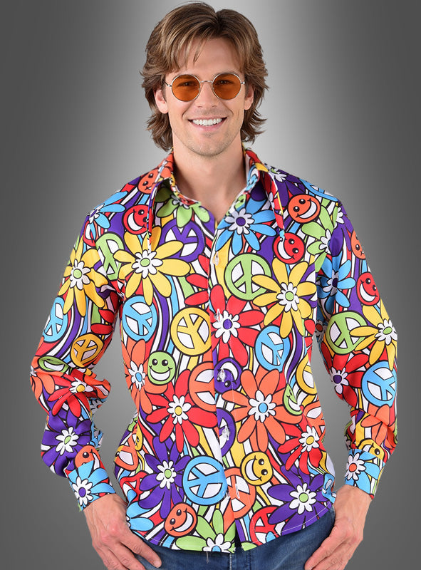 Ein Mann mit runder Sonnenbrille und einem farbenfrohen, langärmeligen Hippie-Blumenhemd für Herren „Smile“ mit einem von den 1960er Jahren inspirierten Muster aus Blumen, Peace-Zeichen und Smileys steht vor einem grauen Hintergrund mit Farbverlauf. Dieses farbenfrohe Hemd ist das perfekte Herrenkostüm für alle, die den authentischen Stil der 70er Jahre verkörpern möchten.