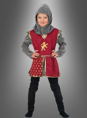 Ein Kind, das das Ritterkostüm „Leon Kinder Mittelalter“ trägt, steht vor einem einfarbigen Hintergrund mit Farbverlauf. Es ist mit einer roten Tunika mit goldenem Löwenwappen, einer schwarzen Hose und einer grauen Kapuze bekleidet.