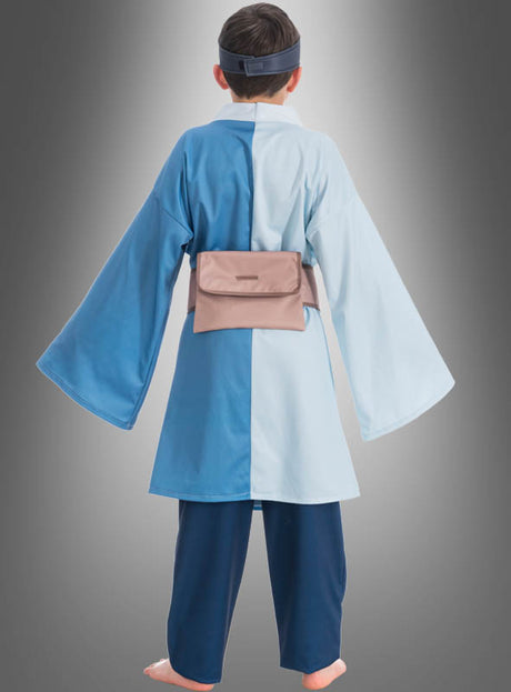 Ein Kind steht barfuß mit dem Rücken zur Kamera und trägt das Mitsuki-Kostüm aus dem Anime „Boruto“ – eine blaue und hellblaue Robe mit passender Hose, Stirnband und hellbrauner Gürteltasche – vor einem grauen Hintergrund mit Farbverlauf, wodurch ein authentisches „Boruto“-Cosplay perfekt zur Geltung kommt.