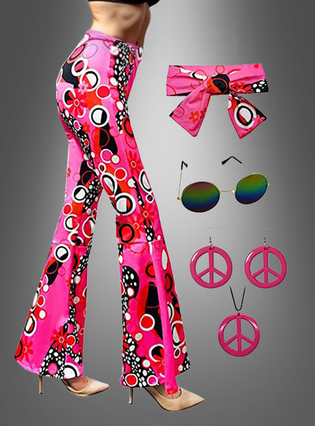 Eine Frau präsentiert die „Hippie-Schlaghose“ mit Accessoires: dazu gehören trendige rosa und mehrfarbige Schlaghosen, kombiniert mit einem passenden Stirnband, einer runden Sonnenbrille und rosa Peace-Zeichen-Ohrringen – die ideale Wahl für jede Hippie-Mottoparty –, während sie vor einem grauen Hintergrund posiert.