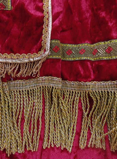 Roter Samtstoff mit goldenen Fransen und einer Zierborte mit geometrischem Muster, hier in Nahaufnahme – ideal, um dem Sankt-Nikolaus-Bischofskostüm oder der Weihnachtsverkleidung einen opulenten Touch zu verleihen.
