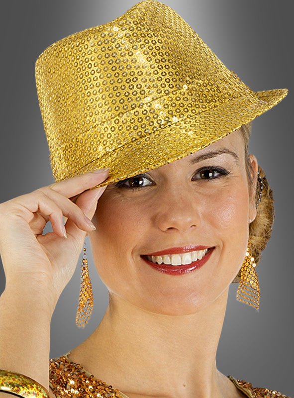 Eine Frau lächelt, während sie den „Pailletten Glitzer Hut Trilby“ aus glänzenden goldenen Pailletten trägt, kombiniert mit passenden Ohrringen und einem Pailletten-Oberteil, vor einem grauen Hintergrund – perfekt als Karnevalsaccessoire.