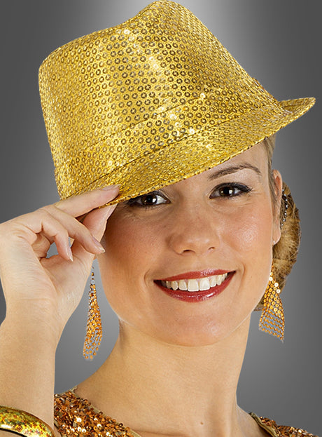 Eine Frau lächelt, während sie den „Pailletten Glitzer Hut Trilby“ aus glänzenden goldenen Pailletten trägt, kombiniert mit passenden Ohrringen und einem Pailletten-Oberteil, vor einem grauen Hintergrund – perfekt als Karnevalsaccessoire.