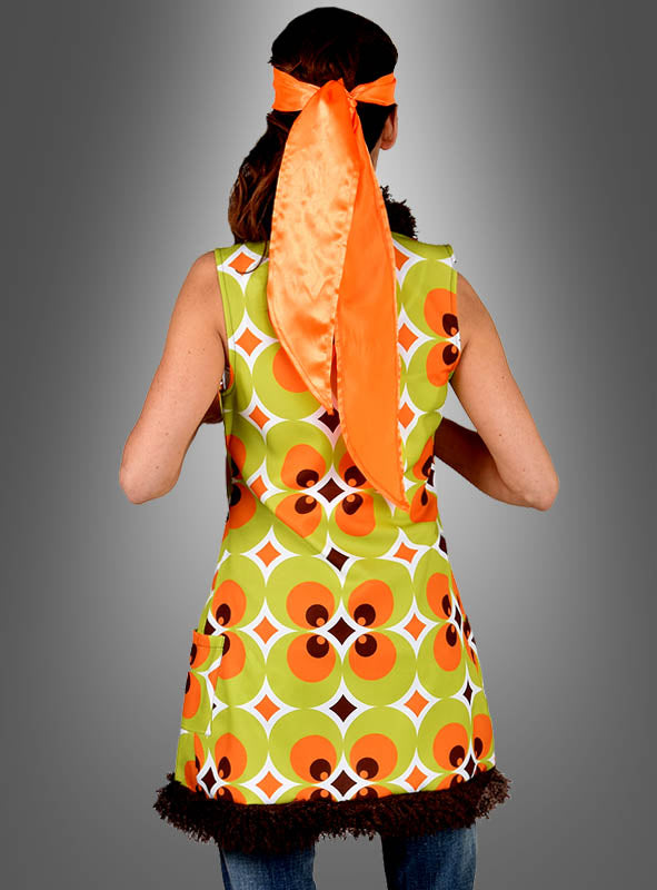 Eine Person, die mit dem Rücken zur Kamera steht und eine ärmellose „70er Retroweste Damen“ in Grün-Braun mit einem Retro-Muster in Grün und Braun trägt, dazu ein orangefarbenes Satin-Kopftuch, das hinten gebunden ist, vor einem grauen Hintergrund mit Farbverlauf.