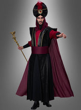 Eine Person, die das „Düsterer Sultan“-Kostüm für Herren trägt – ein schwarz-burgunderrotes, vom Orient inspiriertes Zaubererkostüm, komplett mit Turban, Umhang und Stab –, steht vor einem grauen Hintergrund und streckt eine Hand nach vorne; perfekt für jede „1001 Nacht“-Kostümparty oder jede Karnevalsfeier im Sultan-Stil.