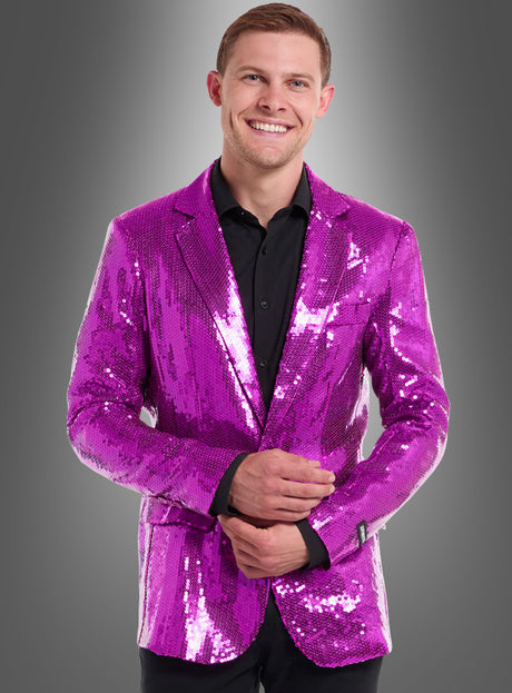 Ein Mann, der eine leuchtend pinkfarbene Pailletten-Jacke für Herren in Pink und ein schwarzes Hemd trägt, steht vor einem grauen Hintergrund mit Farbverlauf und lächelt in die Kamera.