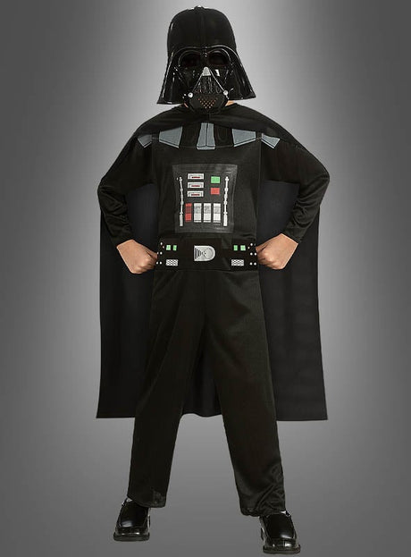 Ein Kind im Darth-Vader-Kinderkostüm steht selbstbewusst mit den Händen in den Hüften vor einem grauen Hintergrund und präsentiert stolz dieses kultige Star-Wars-Kostüm. Als offizielles Lizenzkostüm gibt es den legendären Look aus der Saga originalgetreu wieder.