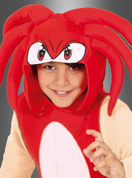 Ein Kind lächelt, während es den „Hedgehog Igel Overall Kinder rot“ trägt, ein rotes Kostüm mit großen Comic-Augen und tentakelartigen Formen auf der Kapuze vor grauem Hintergrund.