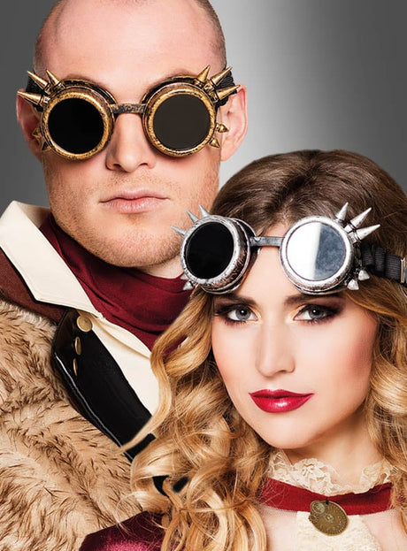 Zwei Personen in braunen und cremefarbenen Steampunk-Outfits mit stacheligen Steampunk-Brillen im Cyber-Look – eine mit kurzen Haaren und eine mit langen, welligen Haaren – posieren selbstbewusst vor einem grauen Hintergrund mit Farbverlauf. Diese auffälligen Details der Kostüm-Accessoires verleihen ihren fantasievollen Looks eine authentische Note.