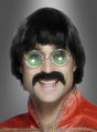 Eine Person, die eine 70er-Beat-Perücke und einen Bart trägt, ergänzt durch eine runde Brille und ein leuchtend rotes Hemd mit goldenem Besatz, lächelt vor einem grauen Hintergrund mit Farbverlauf in die Kamera.