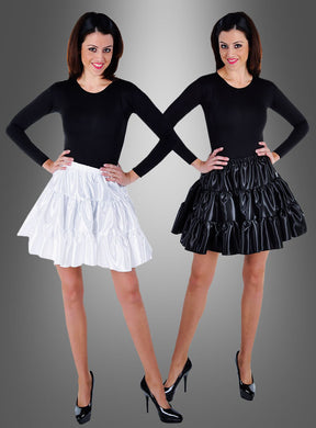 Zwei Frauen posieren nebeneinander, beide tragen ein schwarzes Oberteil mit langen Ärmeln und High Heels; die eine hat ihr Outfit mit einem weißen, blickdichten Satinrock mit Rüschen kombiniert, während die andere denselben Rock in Schwarz trägt, vor einem grauen Hintergrund mit Farbverlauf.