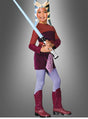 Ein Kind, das ein Ahsoka-Jedi-Kostüm aus „Clone Wars“ von „Star Wars“ trägt und ein blaues Lichtschwert in der Hand hält, steht vor einem grauen Hintergrund und lächelt.