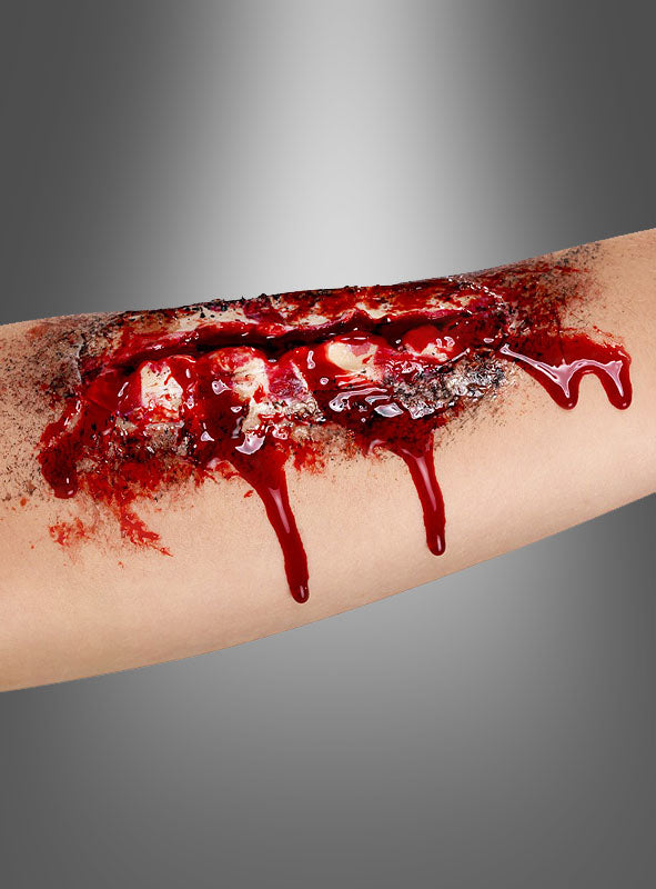 Ein gruseliger Halloween-Make-up-Look entsteht mit dem „Offene Wunde“-Latex mit Kleber, das realistisch wirkendes freiliegendes Gewebe und herabtropfendes Kunstblut zeigt und auf den Unterarm einer Person vor einem grauen Hintergrund aufgebracht wird.